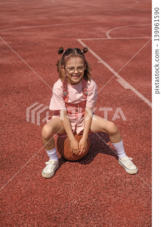 Funny laughing girl with glasses is sitting on a basketball. Sports education and healthy habits Funny laughing girl with glasses is sitting on a basketball. Sports education and healthy habits 139961590