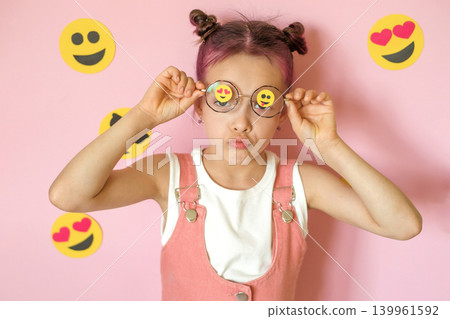 The girl lifts her glasses with emoticons pasted on the lenses, languidly pouting with negative emotions. World Emoji and Social Media Day. The girl lifts her glasses with emoticons pasted on the lenses, languidly pouting with negative emotions. World Emoji and Social Media Day. 139961592