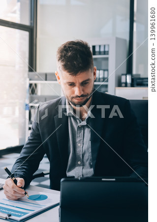 Tired worker. A tired businessman works in the evening. A man in office clothes is holding his temples. Problems in business. The businessman is trying to solve the problems that have arisen. Tired worker. A tired businessman works in the evening. A man in office clothes is holding his temples. Problems in business. The businessman is trying to solve the problems that have arisen. 139961680