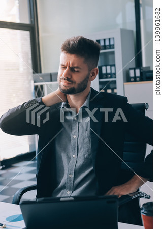 Tired worker. A tired businessman works in the evening. A man in office clothes is holding his temples. Problems in business. The businessman is trying to solve the problems that have arisen. 139961682