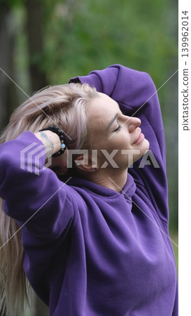 Blonde in purple sweatshirt doing morning exercises, breathing fresh air in forest Blonde in purple sweatshirt doing morning exercises, breathing fresh air in forest 139962014
