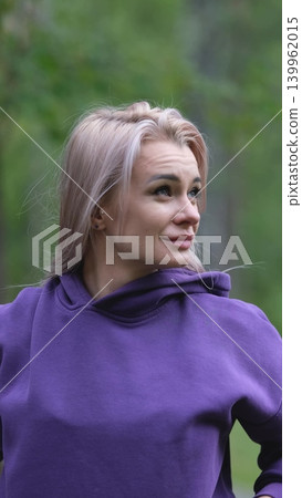 Blonde in purple sweatshirt doing morning exercises, breathing fresh air in forest Blonde in purple sweatshirt doing morning exercises, breathing fresh air in forest 139962015