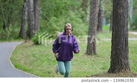 Portrait of young sportswoman jogging during outdoor training in park in the morning. Sport and healthy lifestyle concept Portrait of young sportswoman jogging during outdoor training in park in the morning. Sport and healthy lifestyle concept 139962030