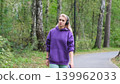 Blonde in purple sweatshirt listening to music on headphones while breathing fresh air in forest 139962033