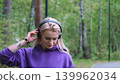 Blonde in purple sweatshirt listening to music on headphones while breathing fresh air in forest 139962034