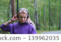 Blonde in purple sweatshirt listening to music on headphones while breathing fresh air in forest 139962035