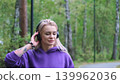 Blonde in purple sweatshirt listening to music on headphones while breathing fresh air in forest 139962036
