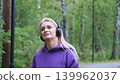 Blonde in purple sweatshirt listening to music on headphones while breathing fresh air in forest 139962037