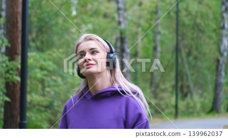 Blonde in purple sweatshirt listening to music on headphones while breathing fresh air in forest 139962037