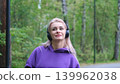 Blonde in purple sweatshirt listening to music on headphones while breathing fresh air in forest 139962038