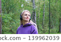 Blonde in purple sweatshirt listening to music on headphones while breathing fresh air in forest 139962039