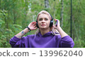 Blonde in purple sweatshirt listening to music on headphones while breathing fresh air in forest 139962040