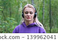 Blonde in purple sweatshirt listening to music on headphones while breathing fresh air in forest 139962041