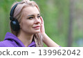 Blonde in purple sweatshirt listening to music on headphones while breathing fresh air in forest 139962042