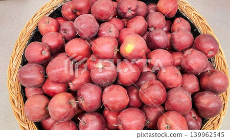 Abundance of fresh ripe red apples displayed in a large wicker basket at a grocery market stall Abundance of fresh ripe red apples displayed in a large wicker basket at a grocery market stall 139962545