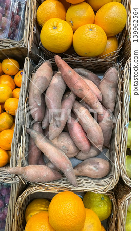 Fresh sweet potatoes and bright oranges displayed in wicker baskets at a grocery store market stall 139962564
