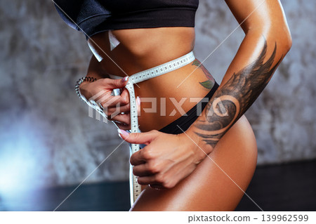 Young slim fitness woman measures waist with a centimeter tattoo on body Young slim fitness woman measures waist with a centimeter tattoo on body 139962599