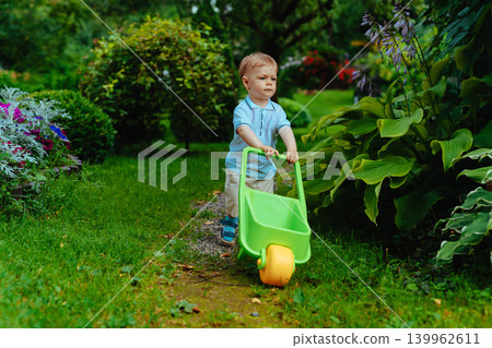 One year cute child in summer garden with wheelbarrow One year cute child in summer garden with wheelbarrow 139962611
