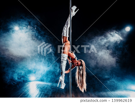 Young woman pole dancing on dark background with blue smoke Young woman pole dancing on dark background with blue smoke 139962619
