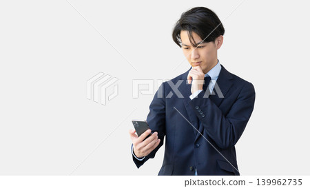 Male businessman thinking while looking at smartphone Male businessman thinking while looking at smartphone 139962735