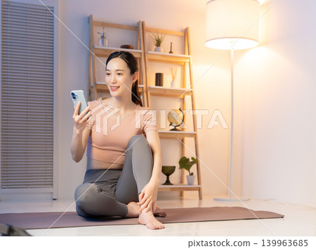 A woman in yoga wear looking at her smartphone at night. 139963685