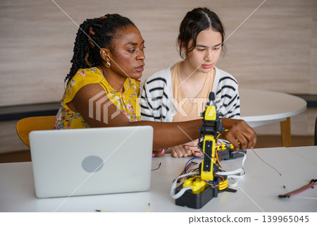 Teacher assists student in operating robotic arm during interactive STEM education activity Teacher assists student in operating robotic arm during interactive STEM education activity 139965045