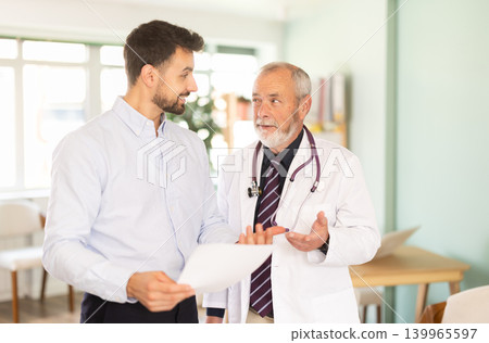 Senior male doctor and man patient examine papers, discuss medical tests result. Senior male doctor and man patient examine papers, discuss medical tests result. 139965597