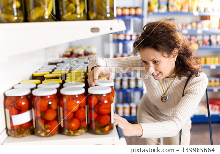 In Russian goods store, woman choose jar of pickled tomatoes In Russian goods store, woman choose jar of pickled tomatoes 139965664