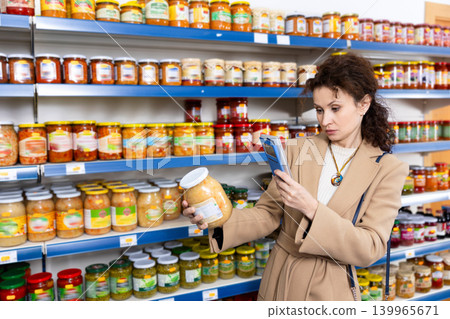 Female shopper scans barcode on jar of sauerkraut using a smartphone while shopping in grocery store Female shopper scans barcode on jar of sauerkraut using a smartphone while shopping in grocery store 139965671