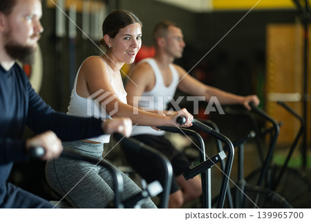 Smiling girl doing cardio training on stationary air bike in gym Smiling girl doing cardio training on stationary air bike in gym 139965700