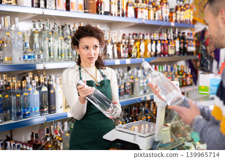 Seller recommends high-quality vodka to man buyer in alcohol department of Russian store Seller recommends high-quality vodka to man buyer in alcohol department of Russian store 139965714