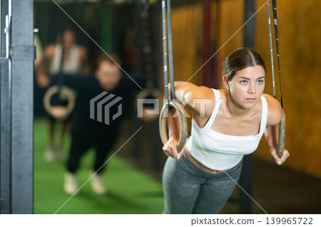 Girl performing chest push-ups with gymnastic rings during workout in gym Girl performing chest push-ups with gymnastic rings during workout in gym 139965722