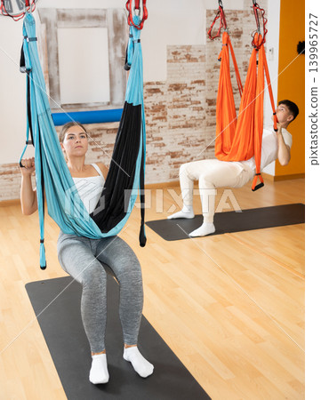 Girl doing aerial pilates exercises with suspended hammock in studio Girl doing aerial pilates exercises with suspended hammock in studio 139965727