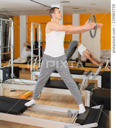 Man stands on reformer and holds ring, hoop in his hands, performs exercises to balance Man stands on reformer and holds ring, hoop in his hands, performs exercises to balance 139965739
