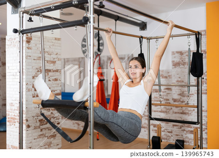 Sporty girl hanging on trapeze table at Pilates workout 139965743