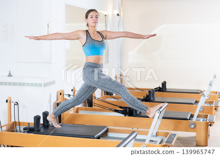 Girl doing stretching exercises on reformer in pilates studio Girl doing stretching exercises on reformer in pilates studio 139965747