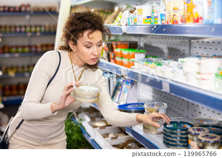 Woman shopper carefully selects salted herring in grocery store Woman shopper carefully selects salted herring in grocery store 139965766