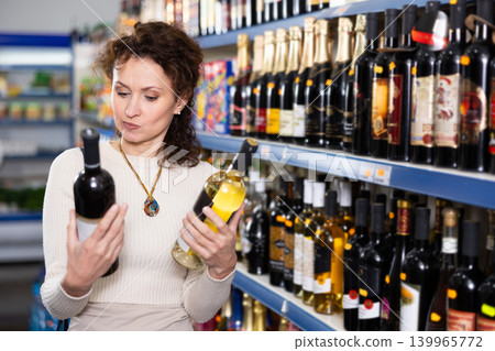 In Russian goods store, woman choose bottle of wine In Russian goods store, woman choose bottle of wine 139965772