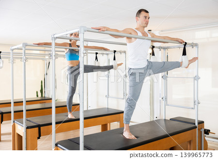 Focused man exercising on trapeze table at group Pilates class Focused man exercising on trapeze table at group Pilates class 139965773