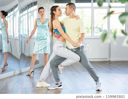 Couple in comfortable sports clothes learns tango dancing during individual lesson Couple in comfortable sports clothes learns tango dancing during individual lesson 139965801