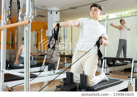 Man in gym with help of rope reformer performs exercises to strengthen muscles of arms 139965820