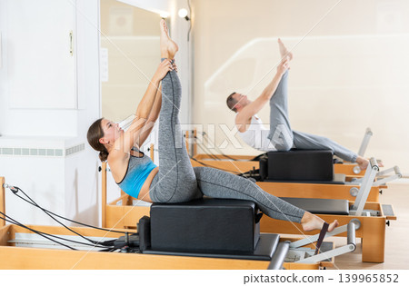 Girl doing exercises on reformer using sitting box in pilates studio Girl doing exercises on reformer using sitting box in pilates studio 139965852
