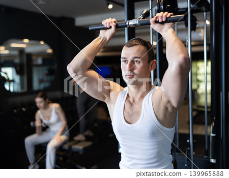Slender athletic man work out muscles of arms and shoulders on simulator in gym of fitness club 139965888
