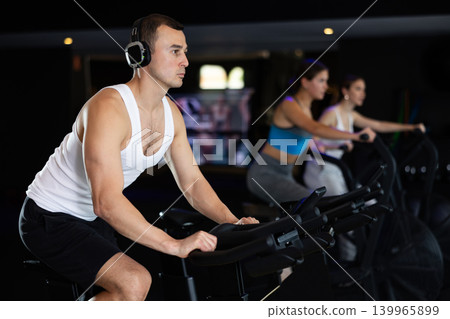 Man in earphone performs exercises with stationary bicycle in gym 139965899