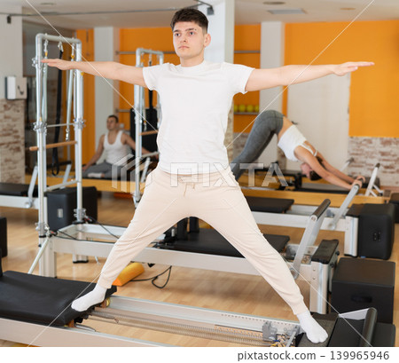Man stands on reformer and performs exercises to balance Man stands on reformer and performs exercises to balance 139965946