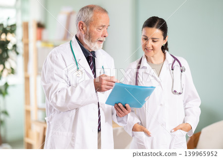 Elderly man and adult woman doctors discussing patient test results Elderly man and adult woman doctors discussing patient test results 139965952