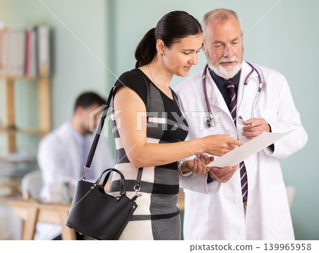 Senior doctor discusses medical tests with happy woman in clinic Senior doctor discusses medical tests with happy woman in clinic 139965958