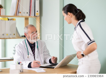 Adult female patient complaining of stomach pain to male doctor Adult female patient complaining of stomach pain to male doctor 139965964