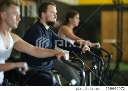 Sportive young guy doing air bike exercises in well-equipped gym 139966072