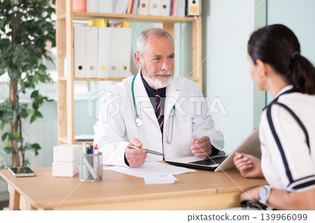 Elderly male doctor talking with adult female patient in medical office Elderly male doctor talking with adult female patient in medical office 139966099
